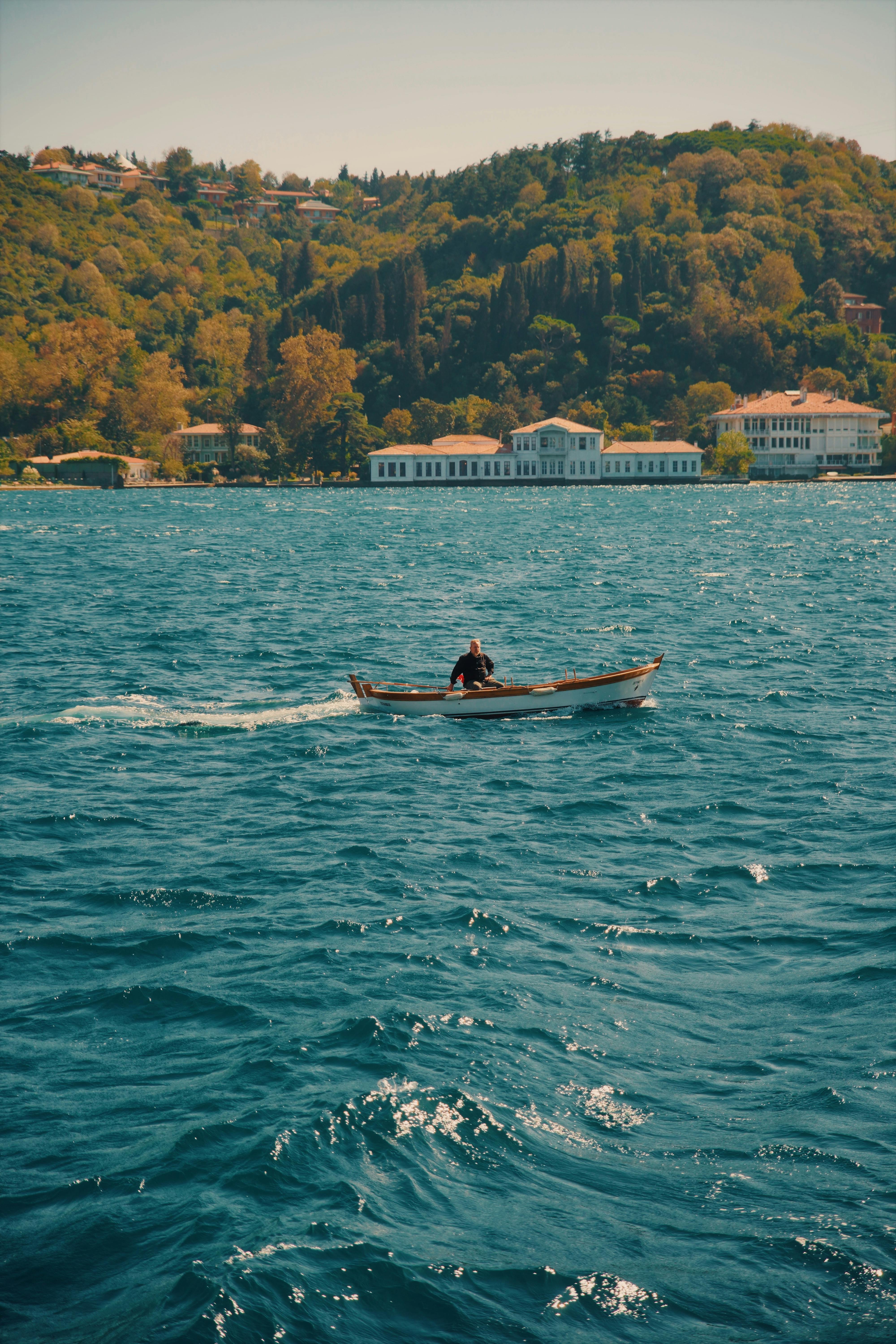一艘单船在郁郁葱葱的山坡建筑附近漂浮，同时充满活力的蓝色水域上