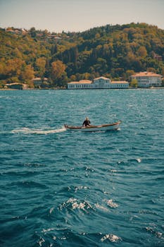一艘单船在郁郁葱葱的山坡建筑附近漂浮，同时充满活力的蓝色水域上