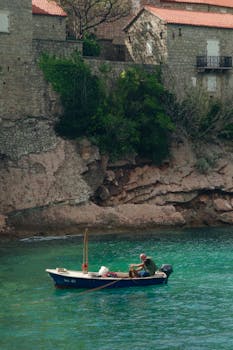孤独的渔民坐在一艘小船上，靠在黑山岩石海岸线上，捕捉到宁静的时刻