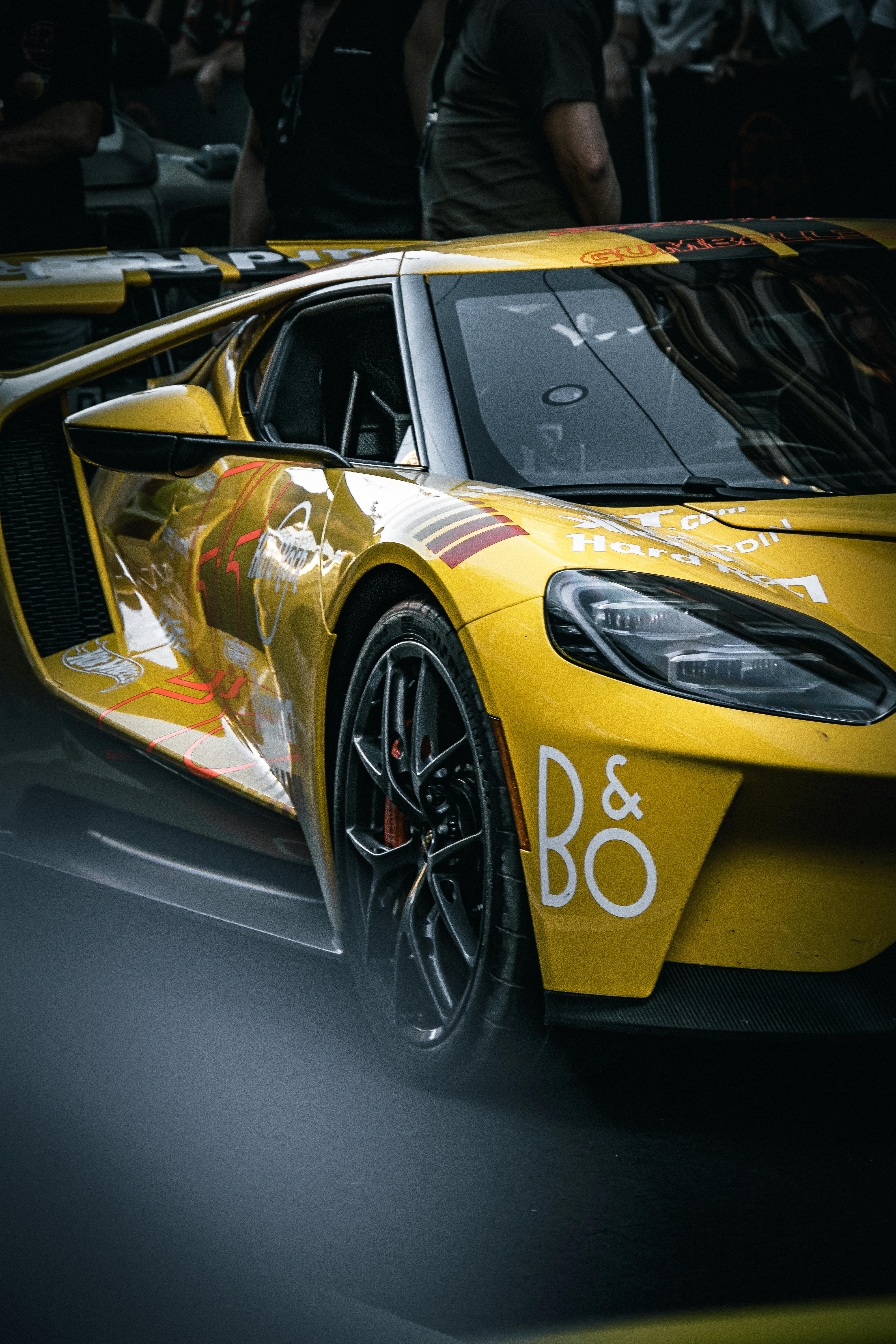 Sleek yellow sports car parked at a nighttime racing event. High-performance, luxury vehicle in low-light setting.