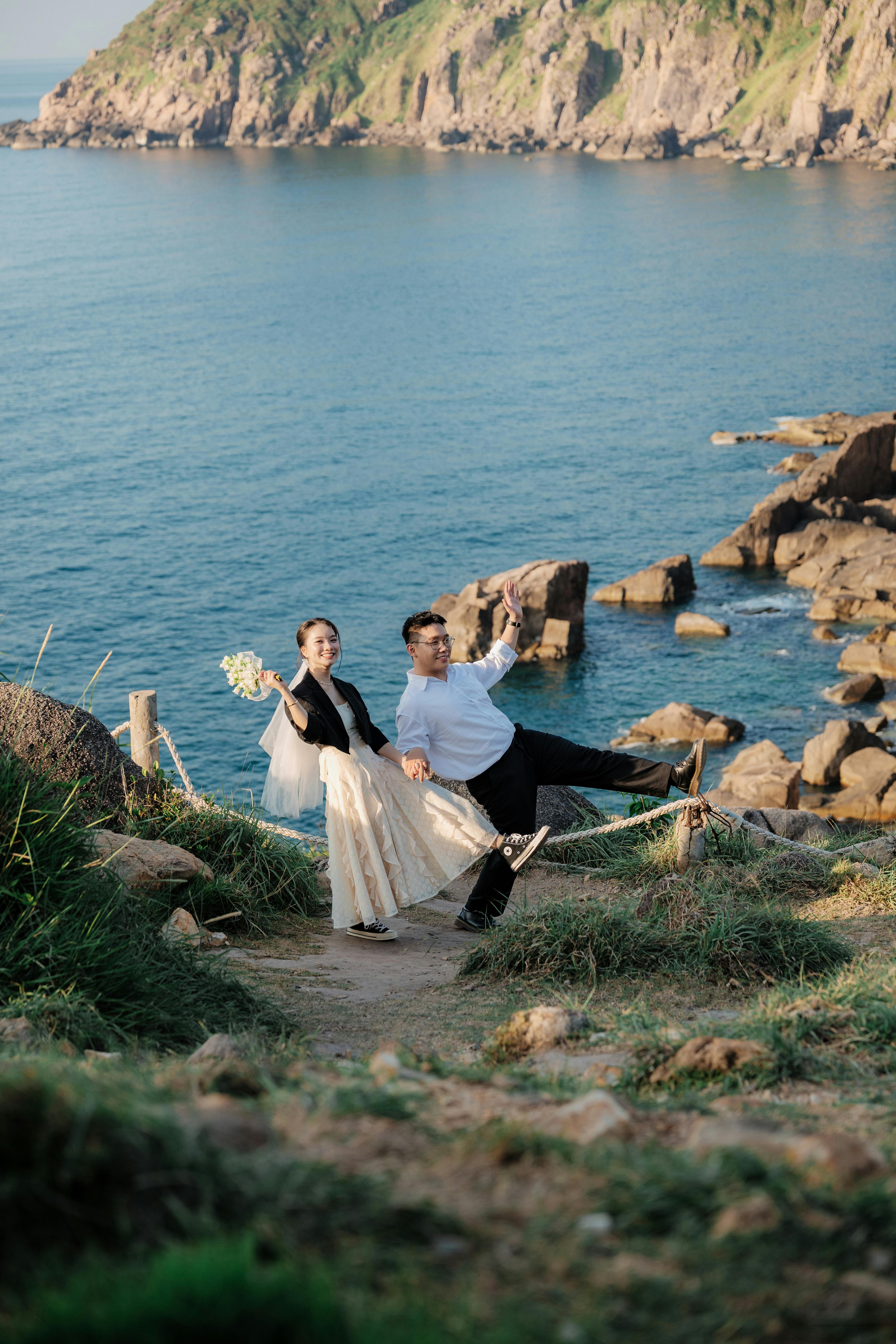 一个快乐的新娘和新郎在海边的岩石海岸线上嬉戏