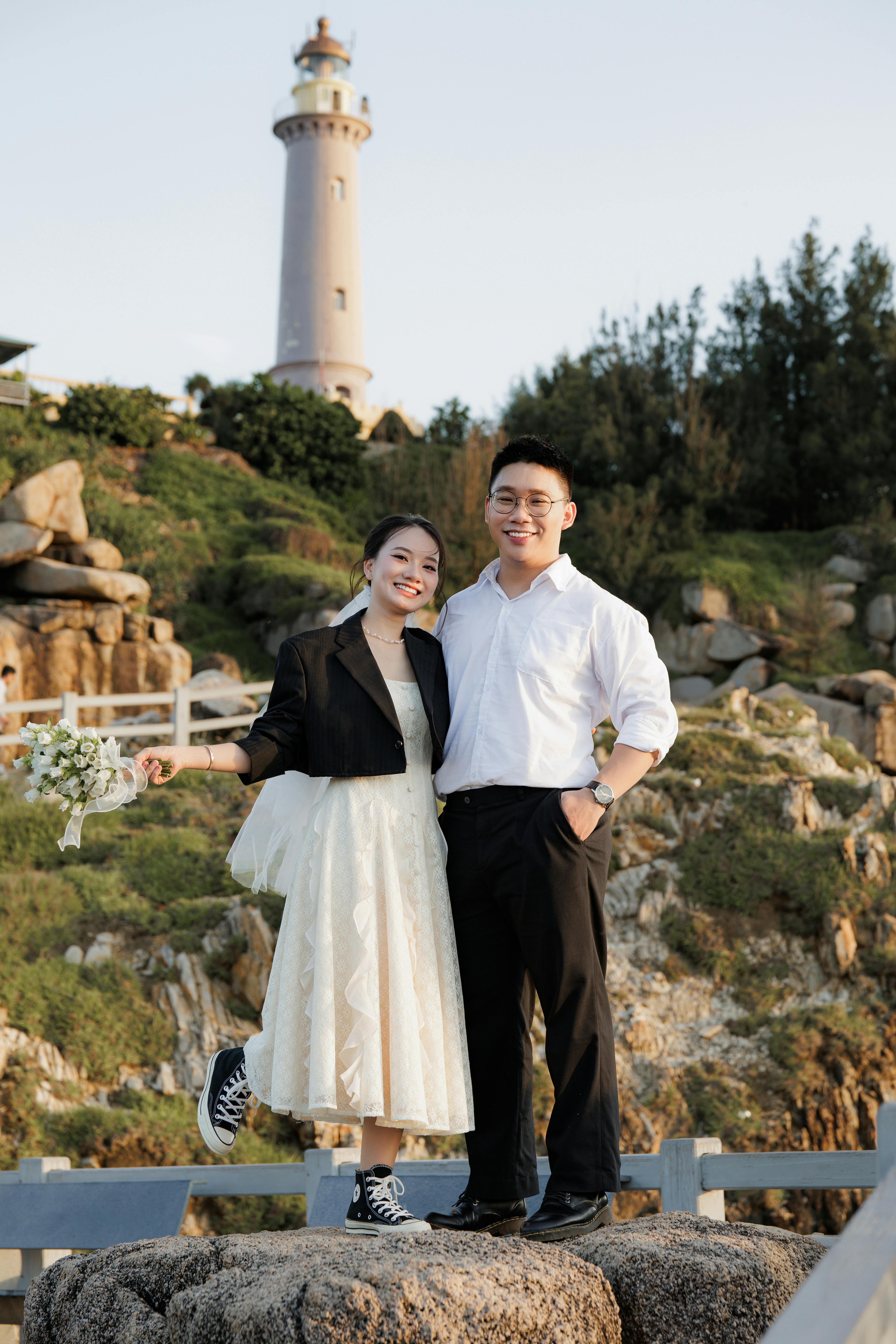 一对开朗的夫妇在背景灯塔的岩石上摆姿势