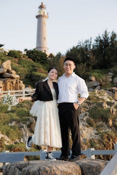 一对开朗的夫妇在背景灯塔的岩石上摆姿势