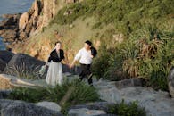 一对衣着优雅的夫妇在岩石海岸的小路上散步，周围被郁郁葱葱的绿色植物和海景包围