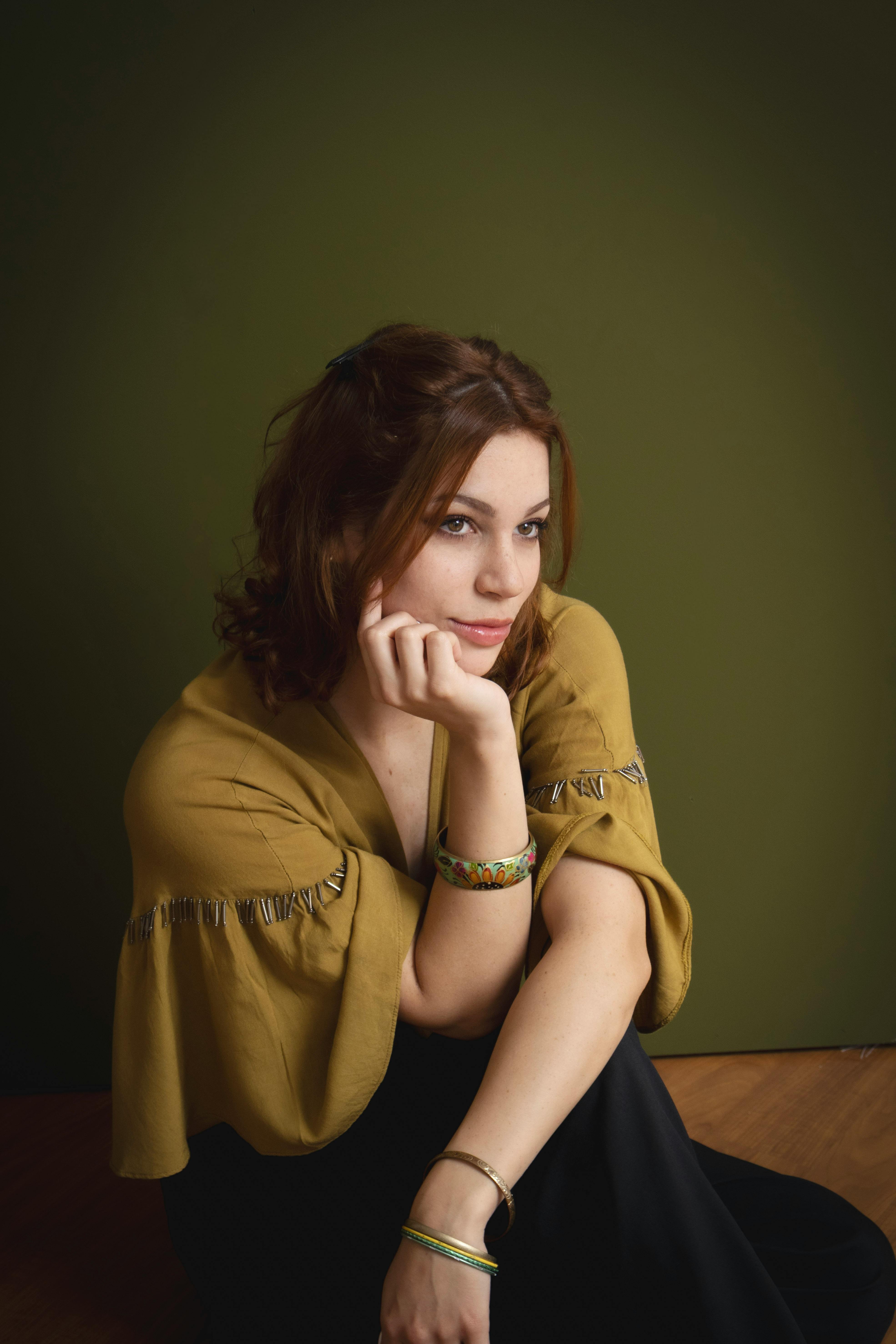 一位女士在深绿色的背景下，穿着绿色围巾，以放松的姿势坐着