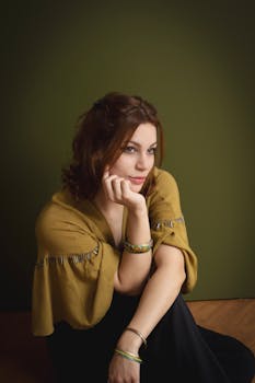 一位女士在深绿色的背景下，穿着绿色围巾，以放松的姿势坐着