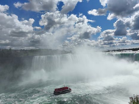 Breathtaking view of Niagara Falls with a tour boat in the mist under a vibrant sky.