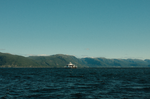 Free Ferry sailing across calm seas with stunning mountain range in the background. Stock Photo