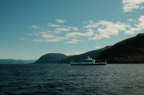Free Passenger ferry traversing a picturesque Norwegian fjord under a blue sky. Stock Photo