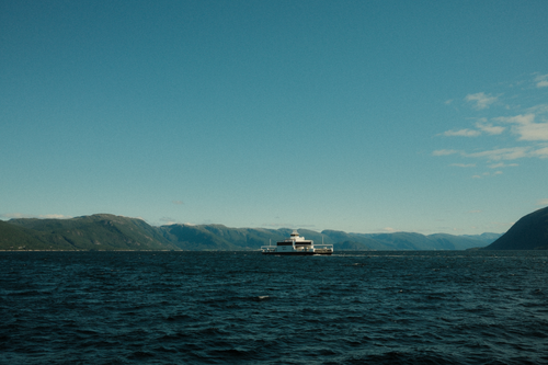 Free A picturesque ferry navigating through the serene Norwegian fjords under a clear blue sky. Stock Photo