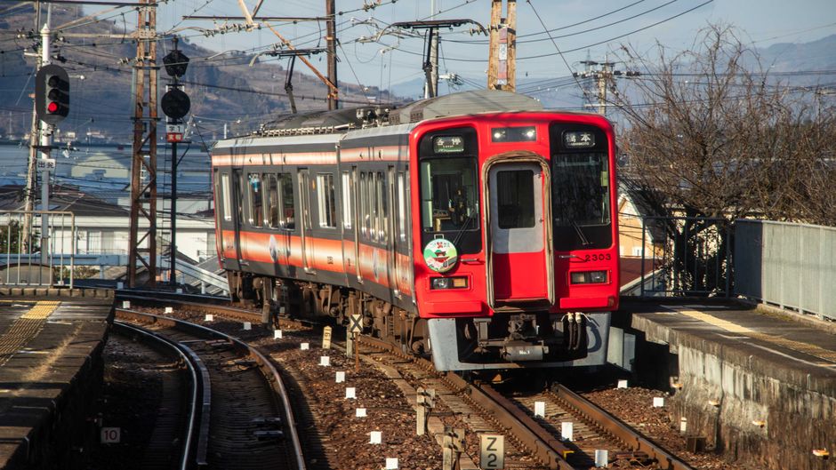 晴れた日に鮮やかな赤い電車が駅に近づき、都市交通の様子を捉えています。