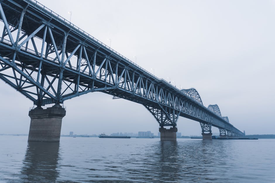 Large steel truss bridge spanning river in Jiujiang, Jiangxi, China, under cloudy sky.
