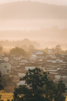 A tranquil village landscape at sunrise with mist enveloping the hills.