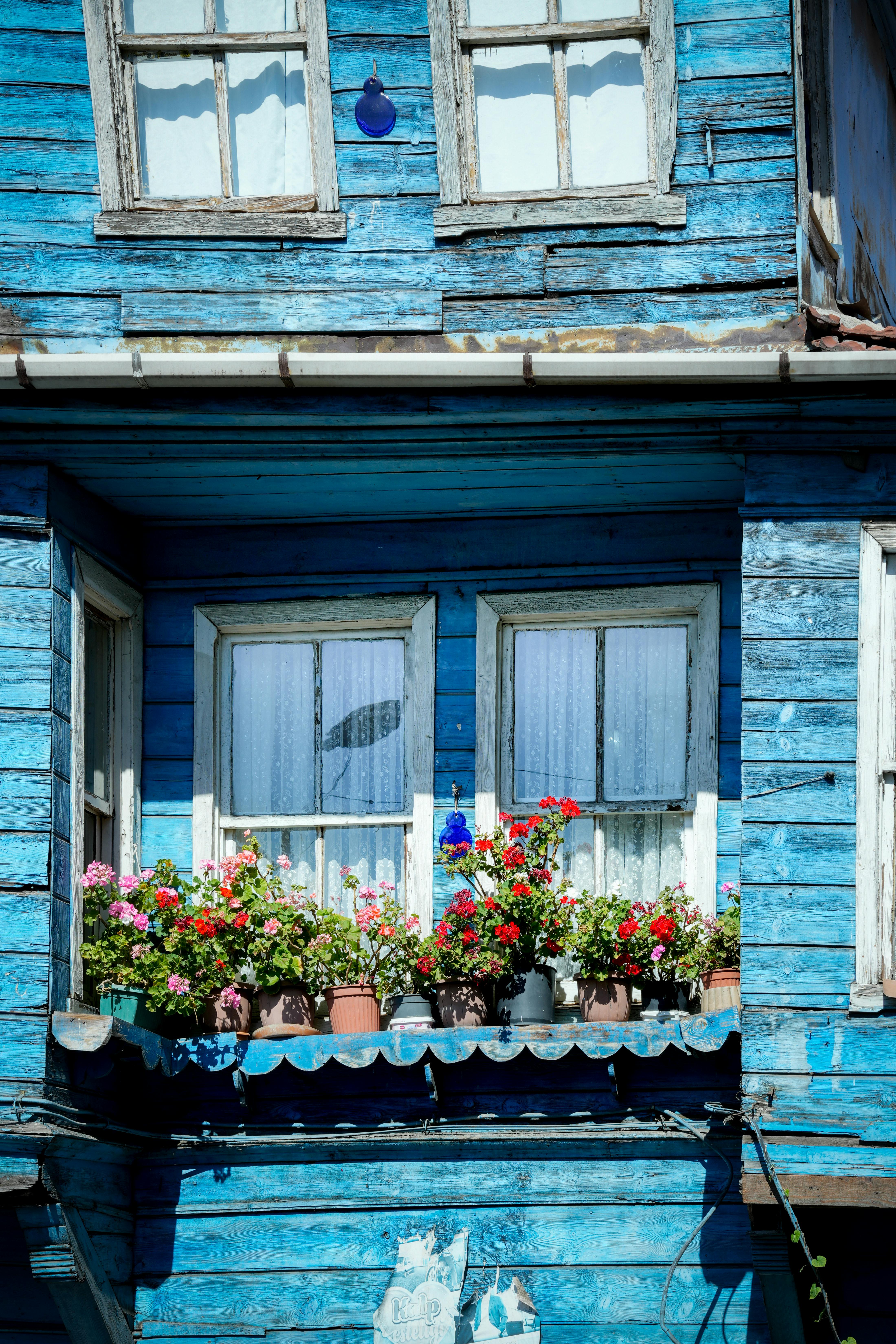 Colorful flowers adorn a wooden balcony of a blue house in İstanbul, Türkiye.