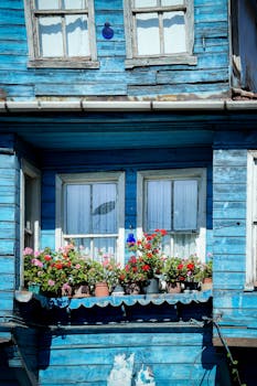 Colorful flowers adorn a wooden balcony of a blue house in İstanbul, Türkiye.