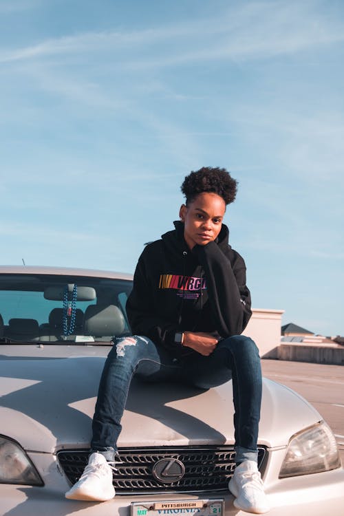 Person Wearing Black Hoodie and Blue Denim Jeans Sitting on Car Hood