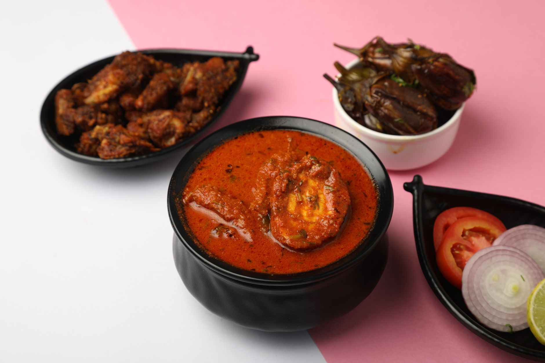 Delicious Indian egg curry with brinjal fry and mutton appetizers, served with sliced onions and tomatoes.