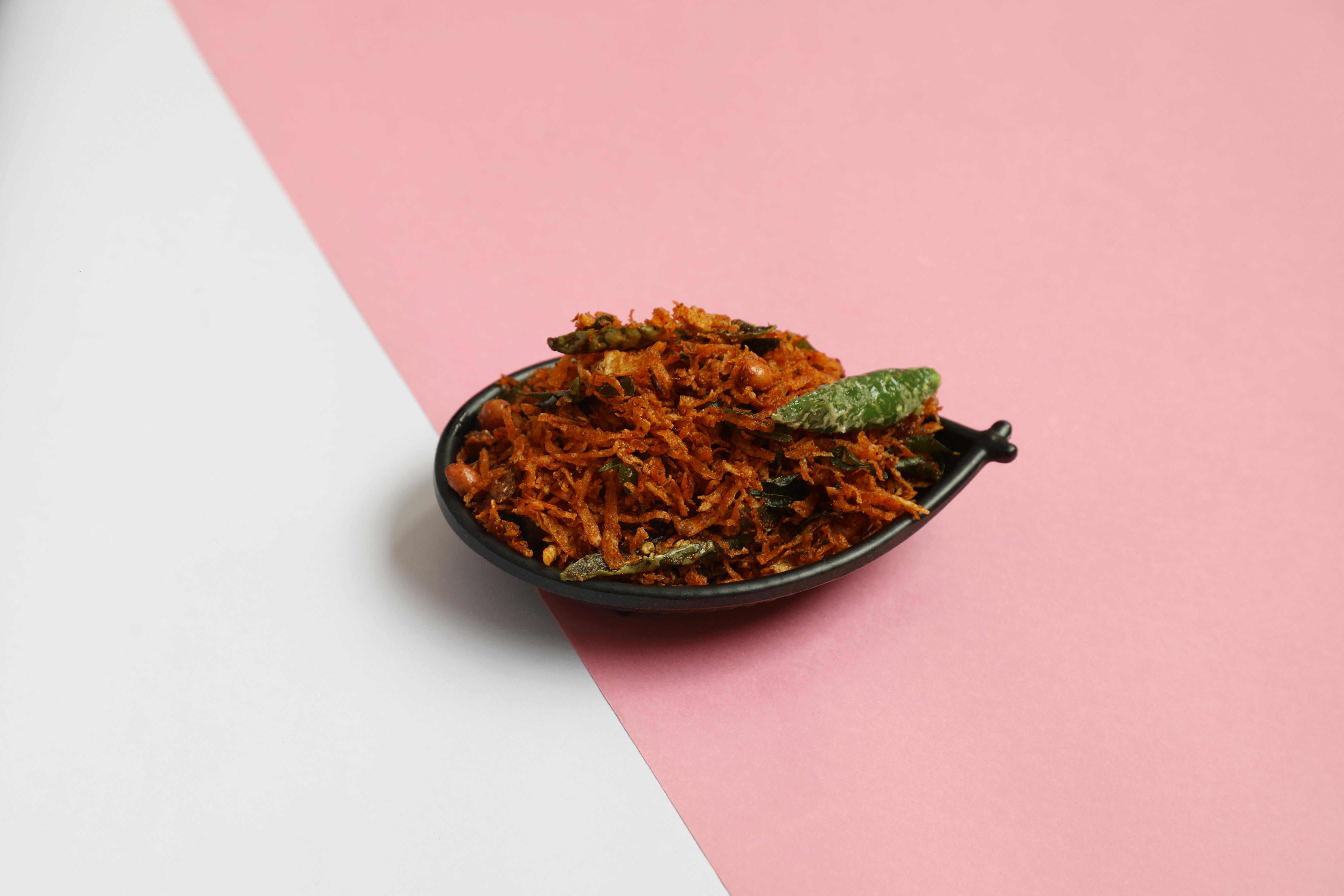 Delicious South Indian crispy snack served in a black bowl against a minimalist pink and white background.