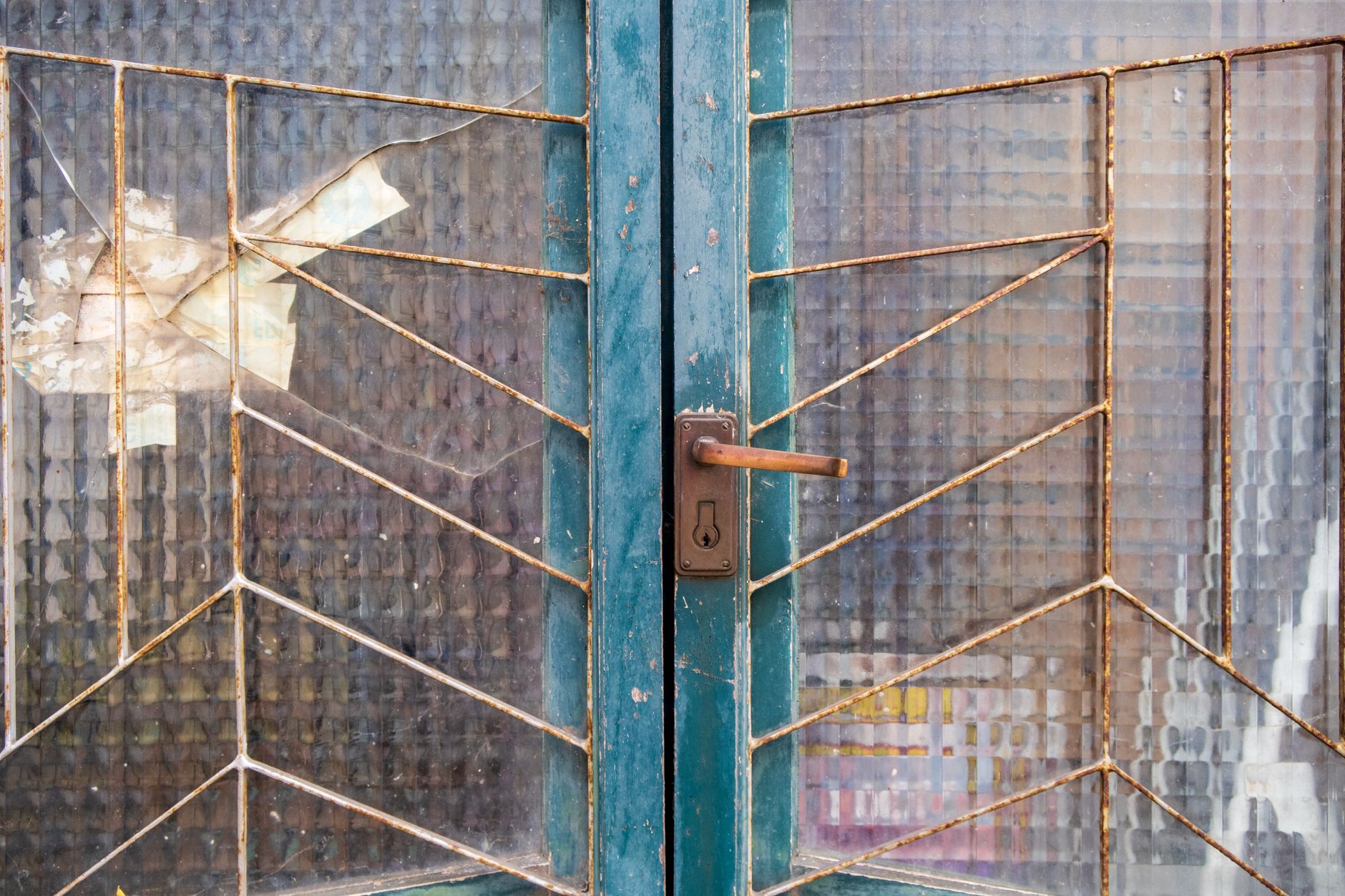 Close-up of an old blue door with rusty metalwork and broken glass panel showcasing decay.