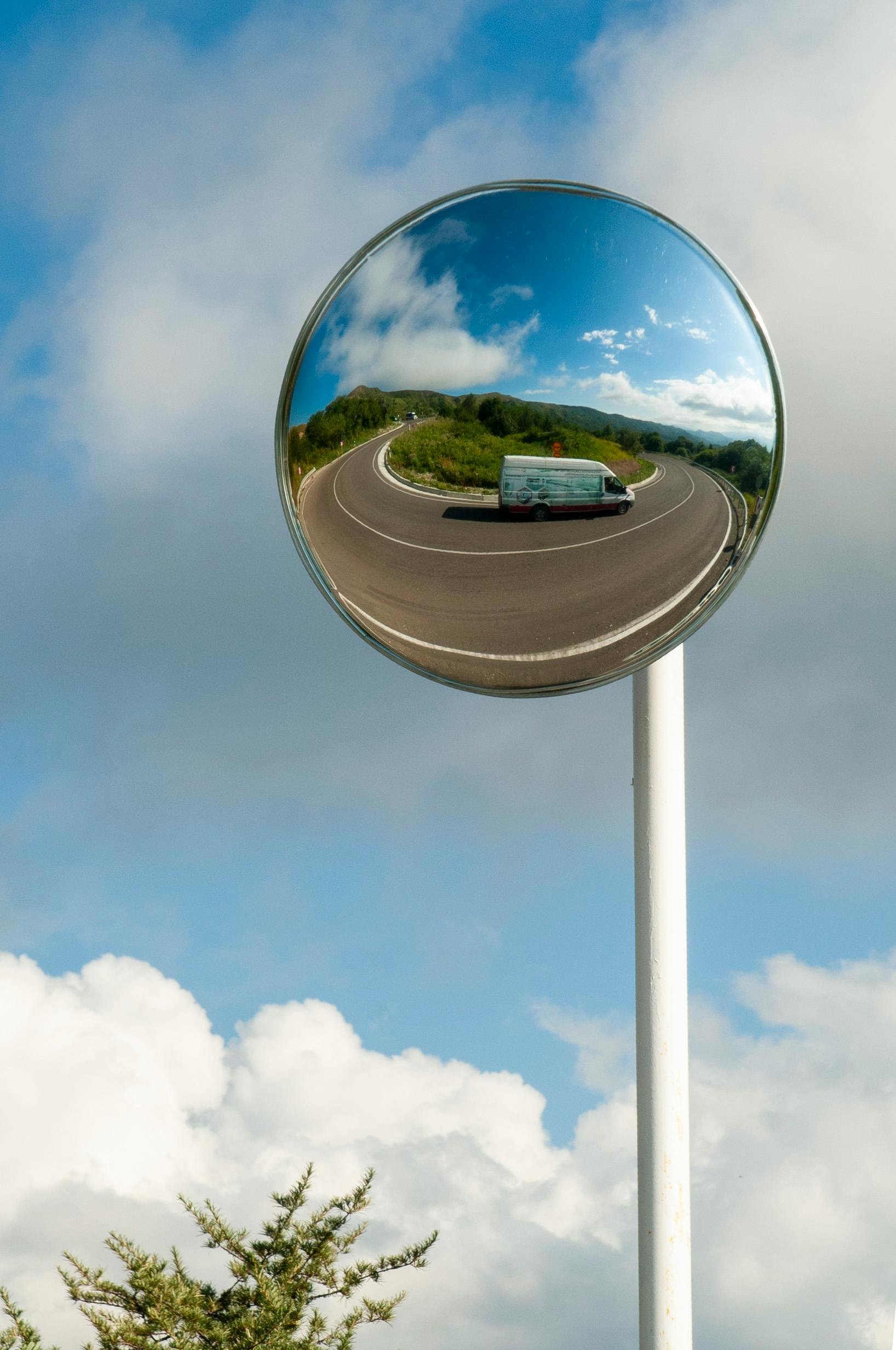 在凸面镜中，晴天反射的车辆捕捉到高速公路的弯曲和蓝天