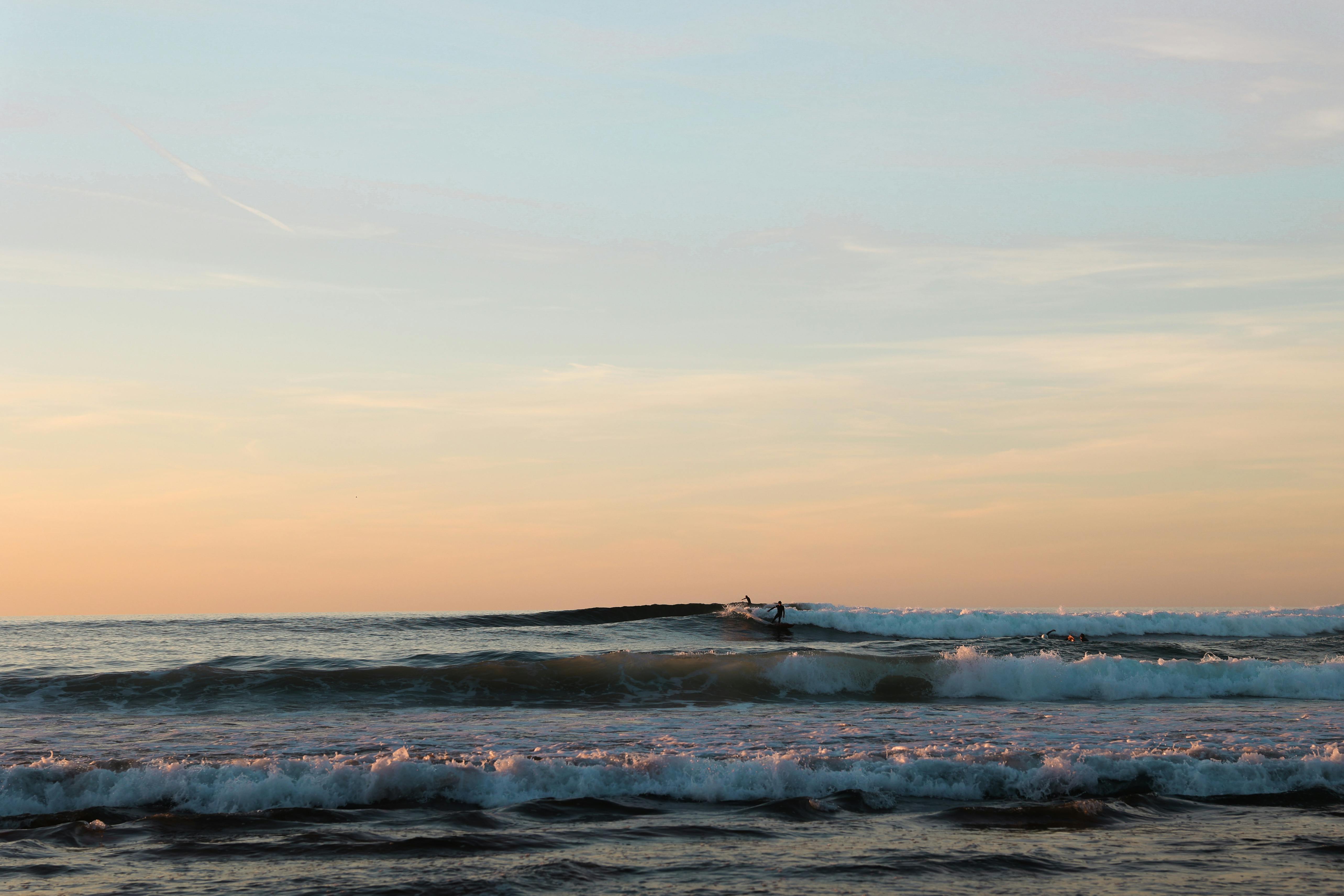 日落时分，巴斯克海岸，冲浪者在宁静的海洋中冲浪