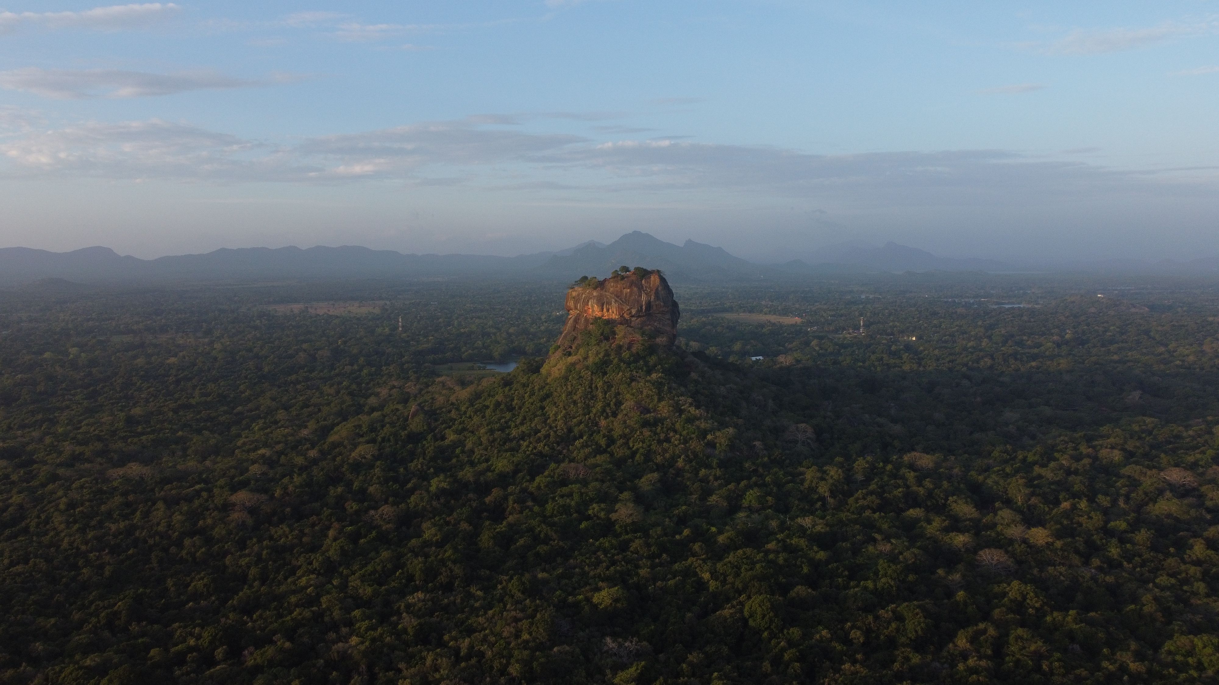 Stunning aerial view of Sigiriya Rock Fortress surrounded by lush forest in Sri Lanka at dawn.