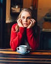 一位穿着红色毛衣的女士，在舒适的咖啡馆里若有所思地凝视着，享用咖啡
