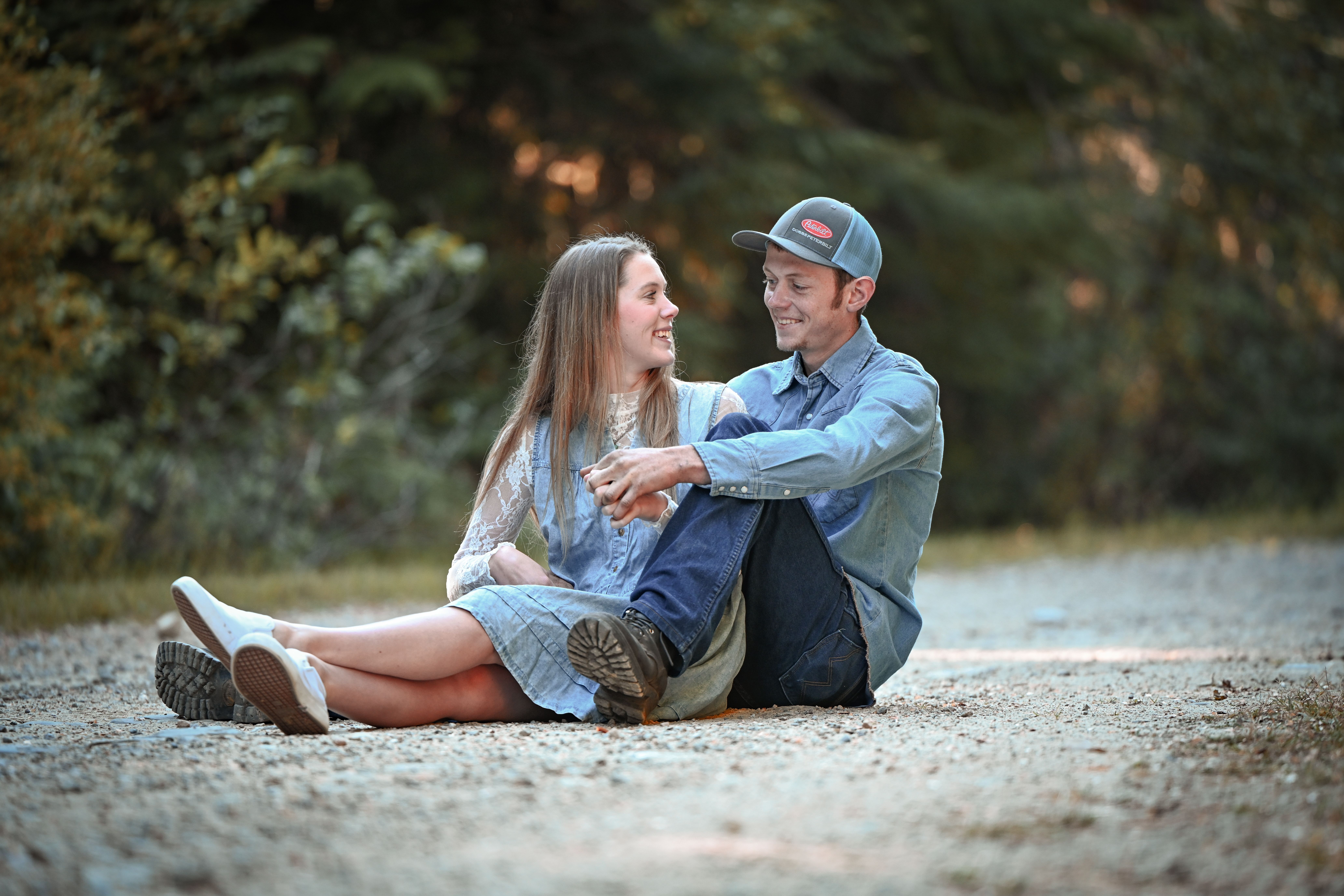 A young couple seated on a gravel path, sharing a joyful moment outdoors in a rural setting.