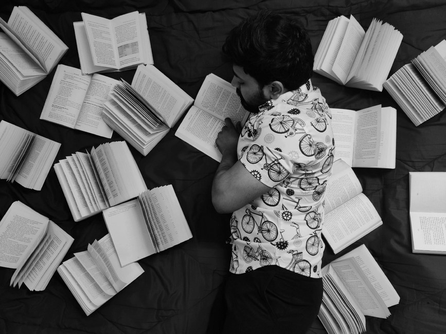 Person surrounded by books, lying on a bed, indulging in a peaceful reading session. Person surrounded by books, lying on a bed, indulging in a peaceful reading session.