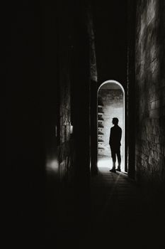 Silhouette of a person standing in a dark, narrow hallway with a light source at the end.