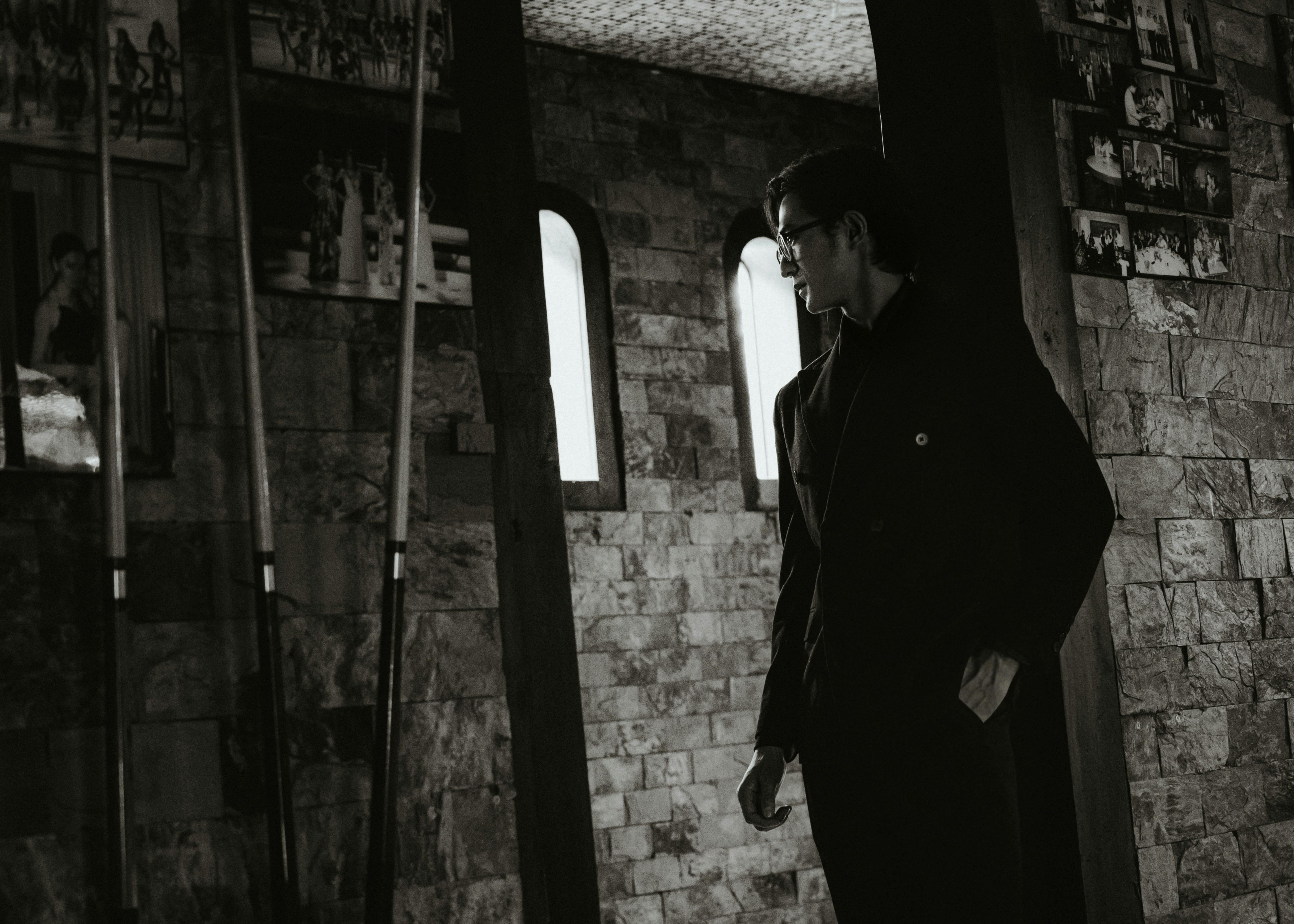 Free Black and white portrait of a man in a rustic indoor setting, exuding a vintage and moody vibe. Stock Photo
