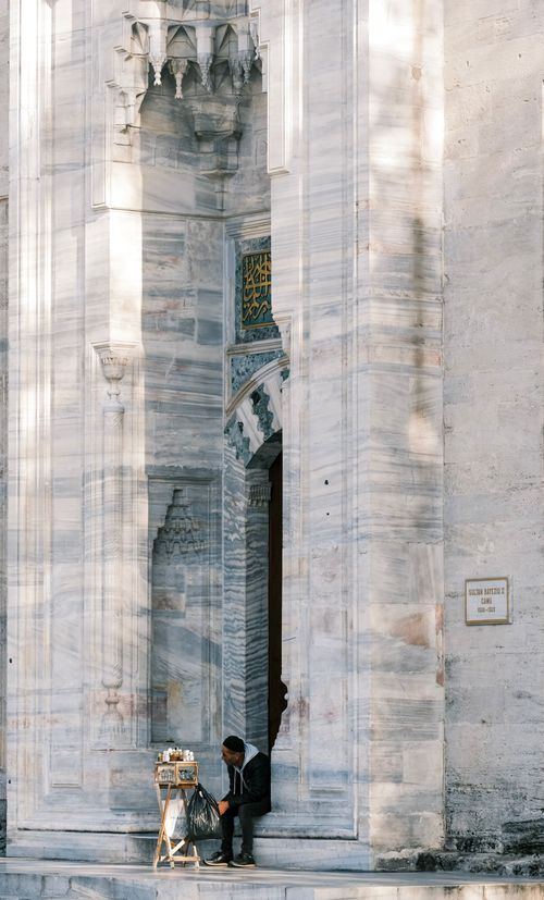 Free A man seated by the grand entrance of a historic mosque, showcasing intricate stone architecture. Stock Photo