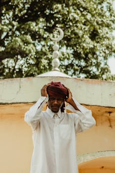 在清真寺附近的户外，一个穿着传统服装的男人正在调整头巾，展示文化遗产