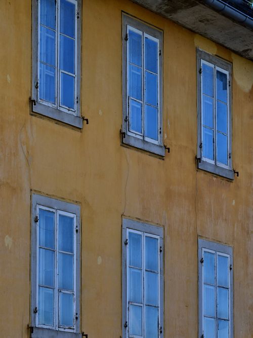 Free Aged yellow building facade with blue-paned symmetrical windows. Stock Photo