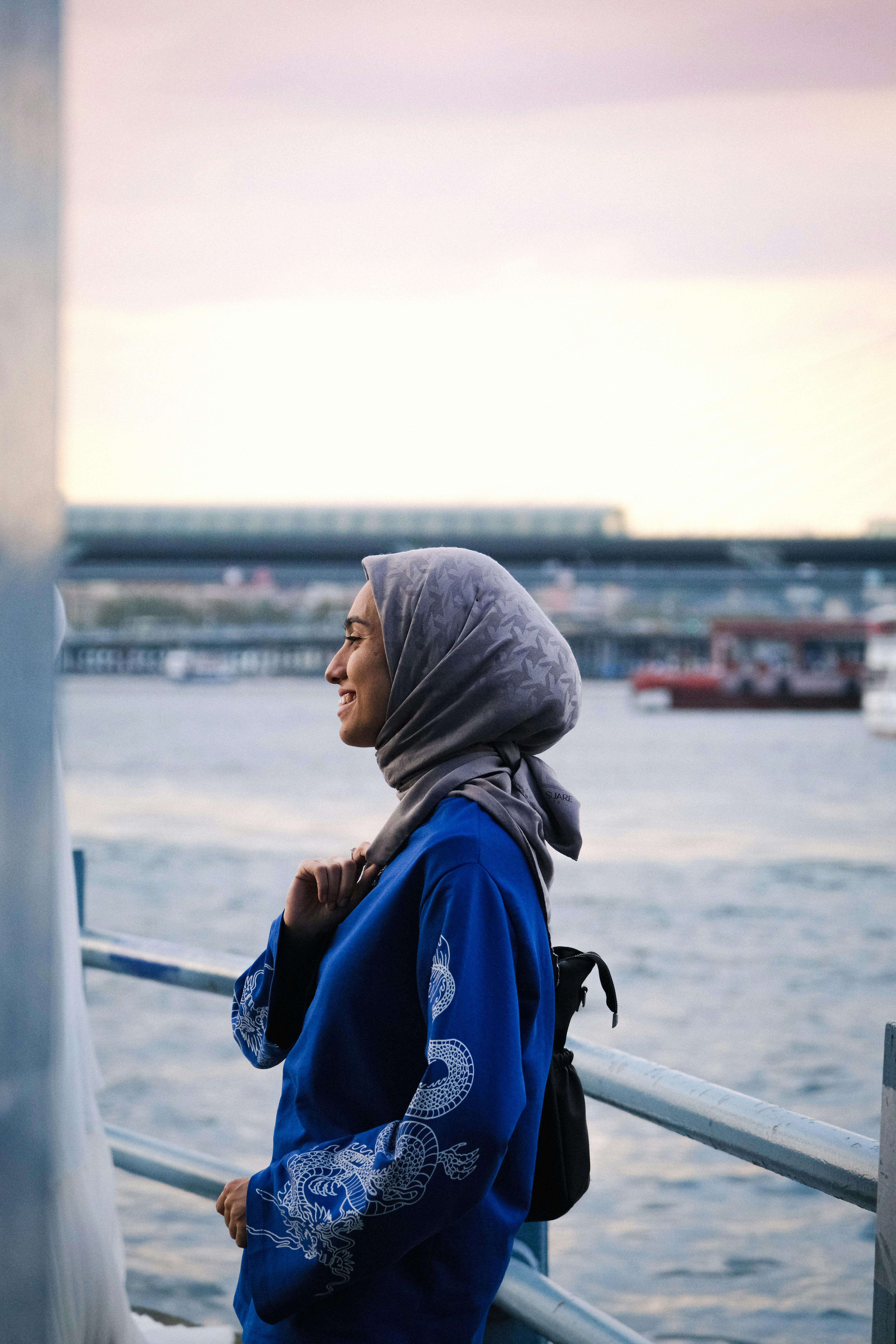 微笑的女人戴着蓝色头巾，在享受日落期间的海滨景色