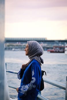 微笑的女人戴着蓝色头巾，在享受日落期间的海滨景色