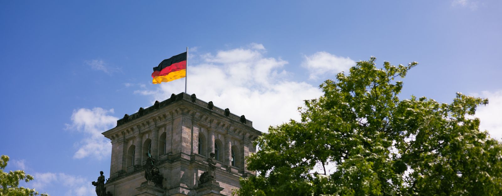 The iconic Reichstag in Berlin with the German flag flying high against a clear blue sky.