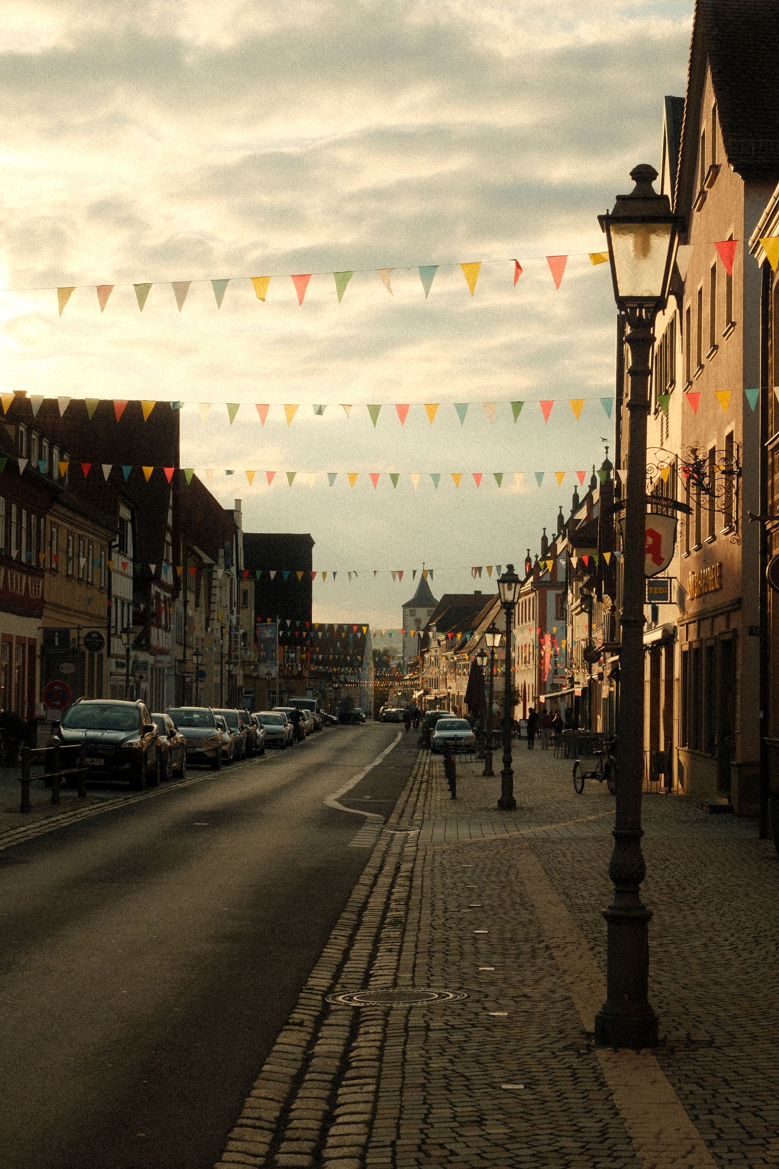 Gratuit O stradă germană pitorească, mărginită de clădiri și ghirlande colorate, sub un cer cald al apusului. Fotografie de stoc