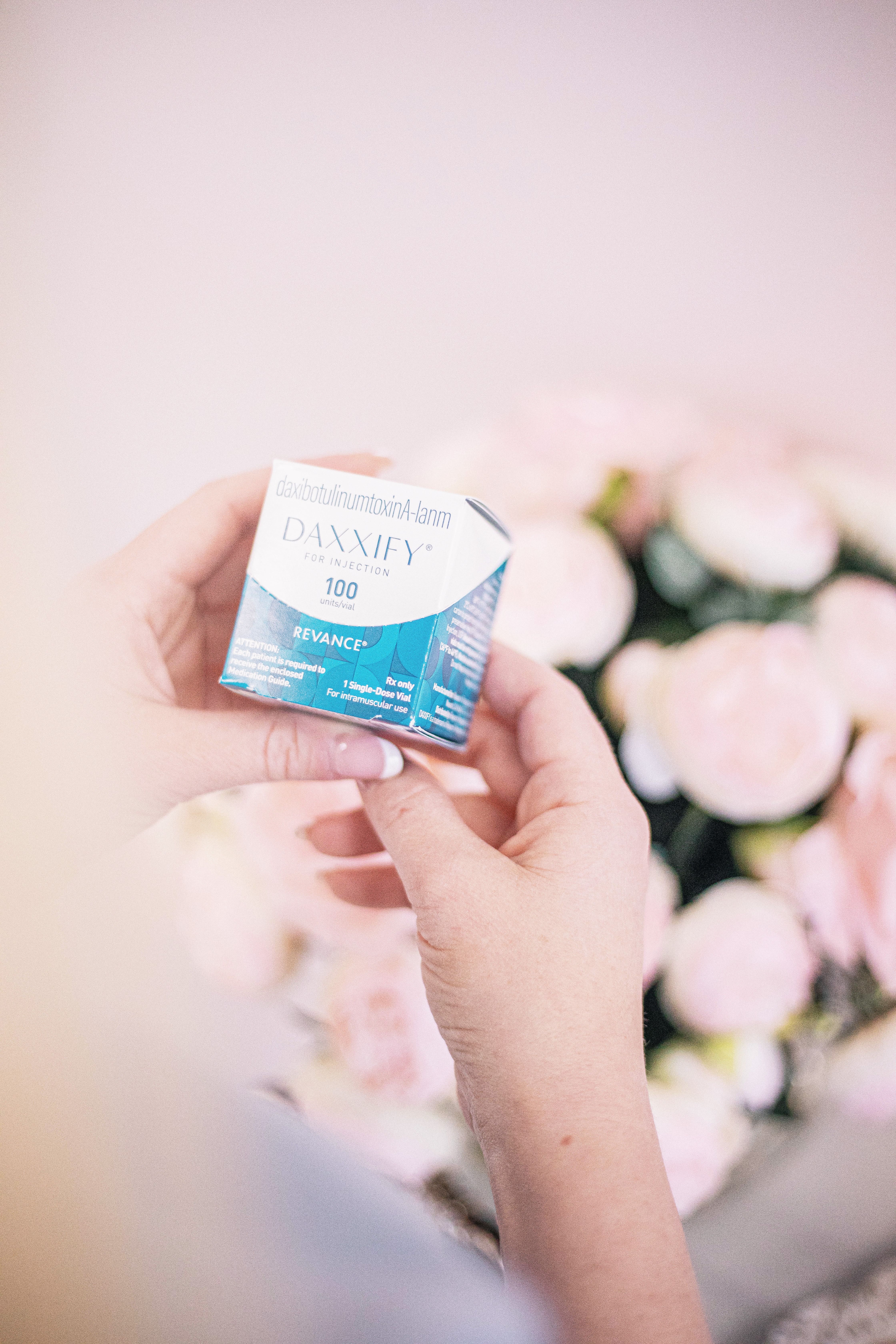 Hands holding a cosmetic product in a spa environment with soft pink tones, symbolizing beauty and care.