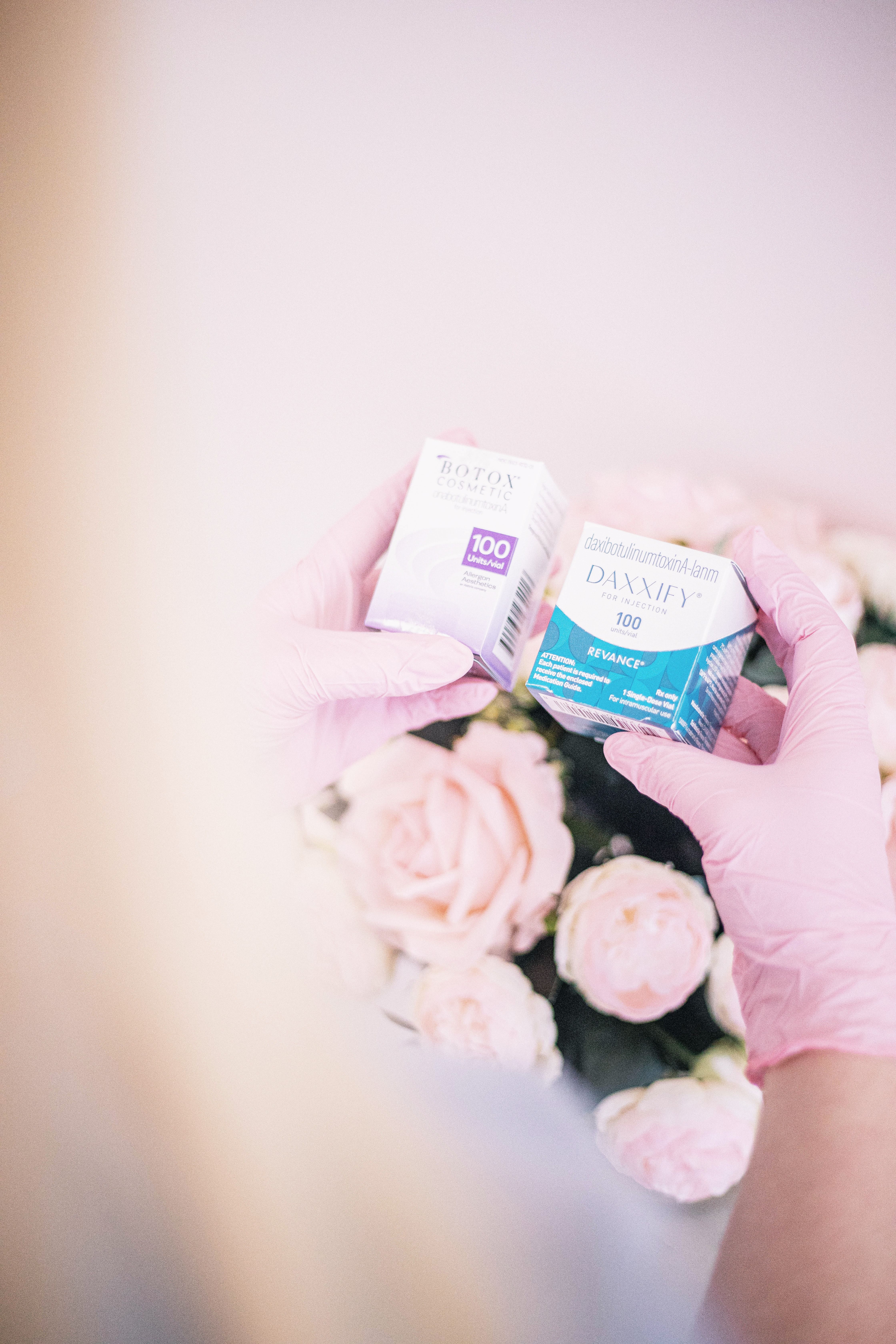 Aesthetic nurse with pink gloves holding beauty products over floral background in spa.