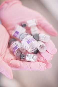 Collection of cosmetic vial bottles held in pink gloves, representing modern beauty treatments.