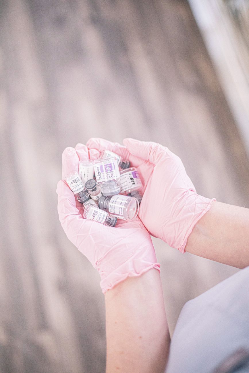 Injectable cosmetic vials held in clinical-grade gloves, symbolic of the blurring line between medical treatment and beauty routine