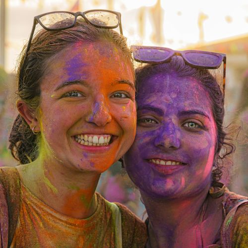 Free Two women joyfully celebrating Holi with colorful powder on their faces outdoors. Stock Photo