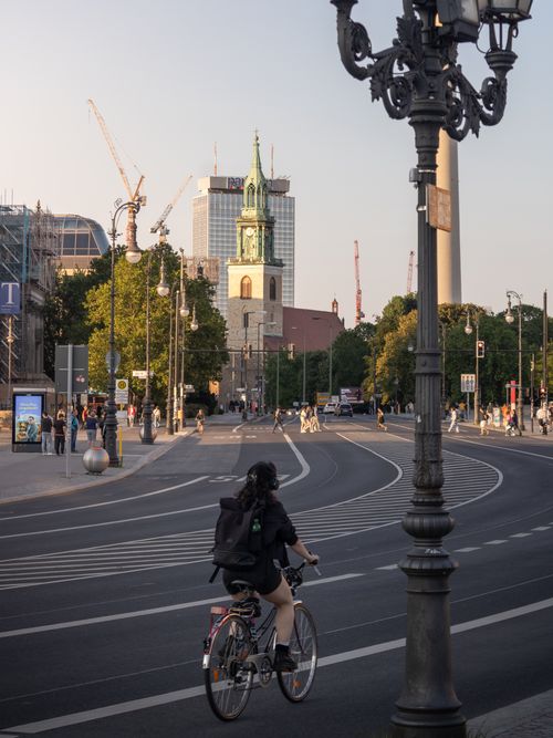 Free A cyclist navigates a bustling street in Berlin, showcasing urban life and iconic architecture at sunset. Stock Photo