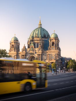 Yellow bus passing in front of the iconic Berlin Cathedral, showcasing motion in a tranquil cityscape.