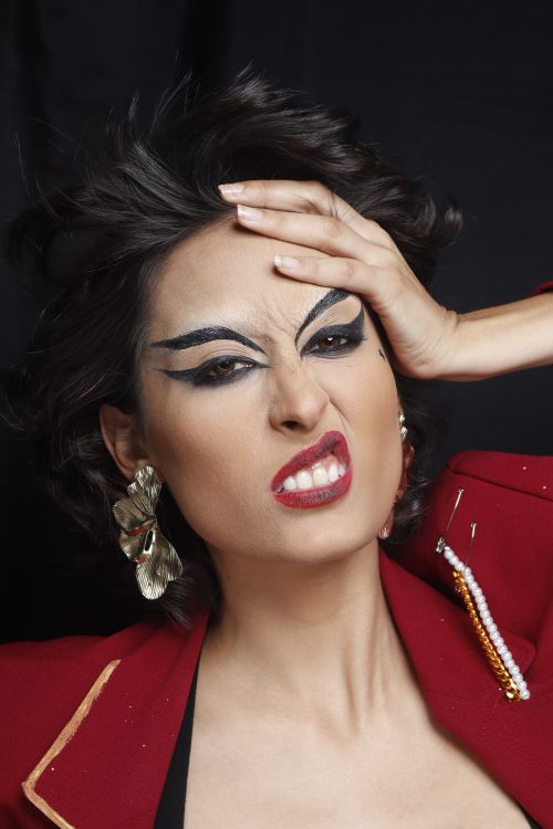 Free Close-up of a woman with bold makeup and expressive facial expression, wearing a red jacket and statement earrings. Stock Photo