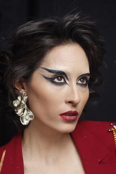 Close-up portrait of a woman with dramatic eye makeup and elegant earrings.