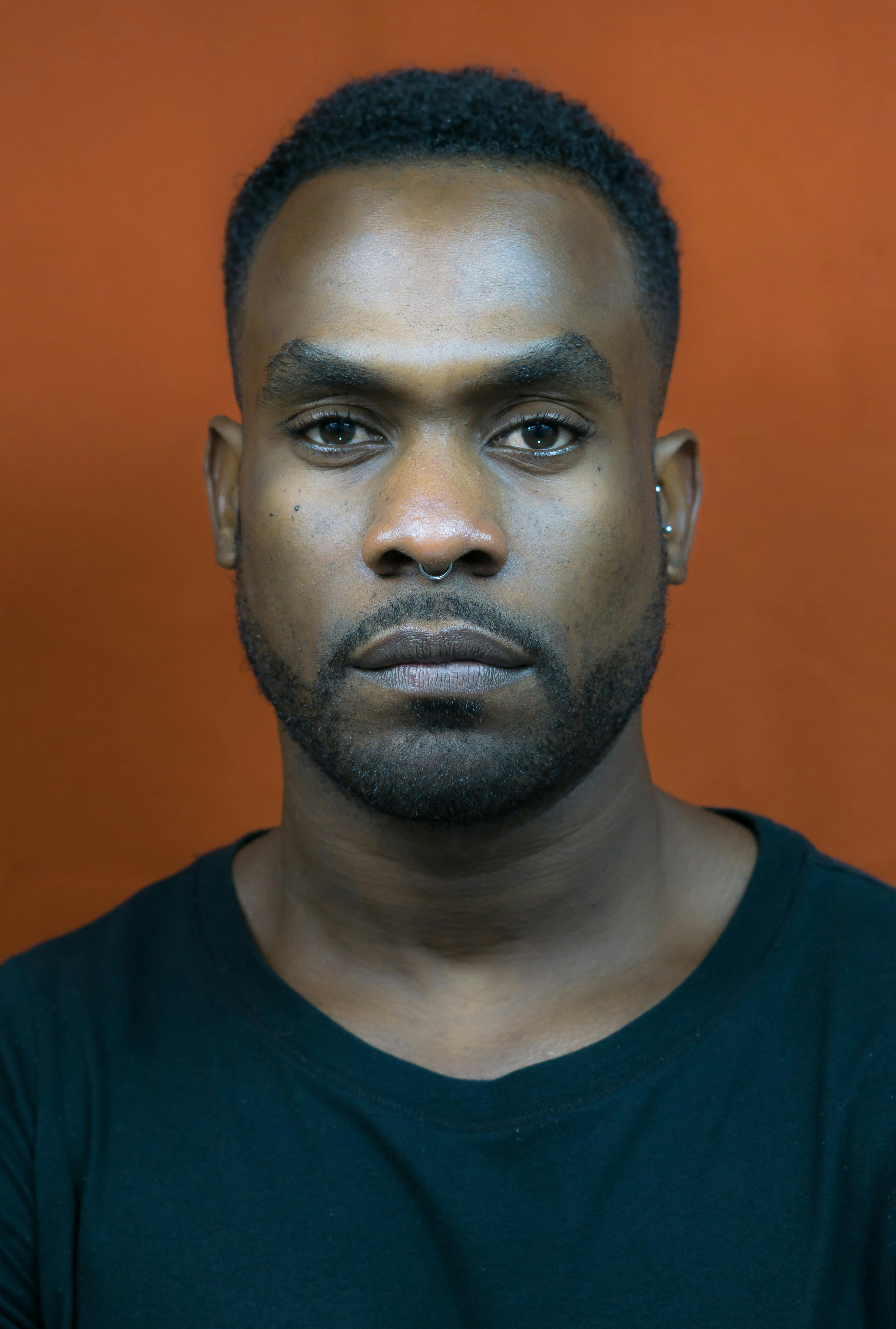 A close-up portrait of a man with a neutral expression against an orange backdrop.