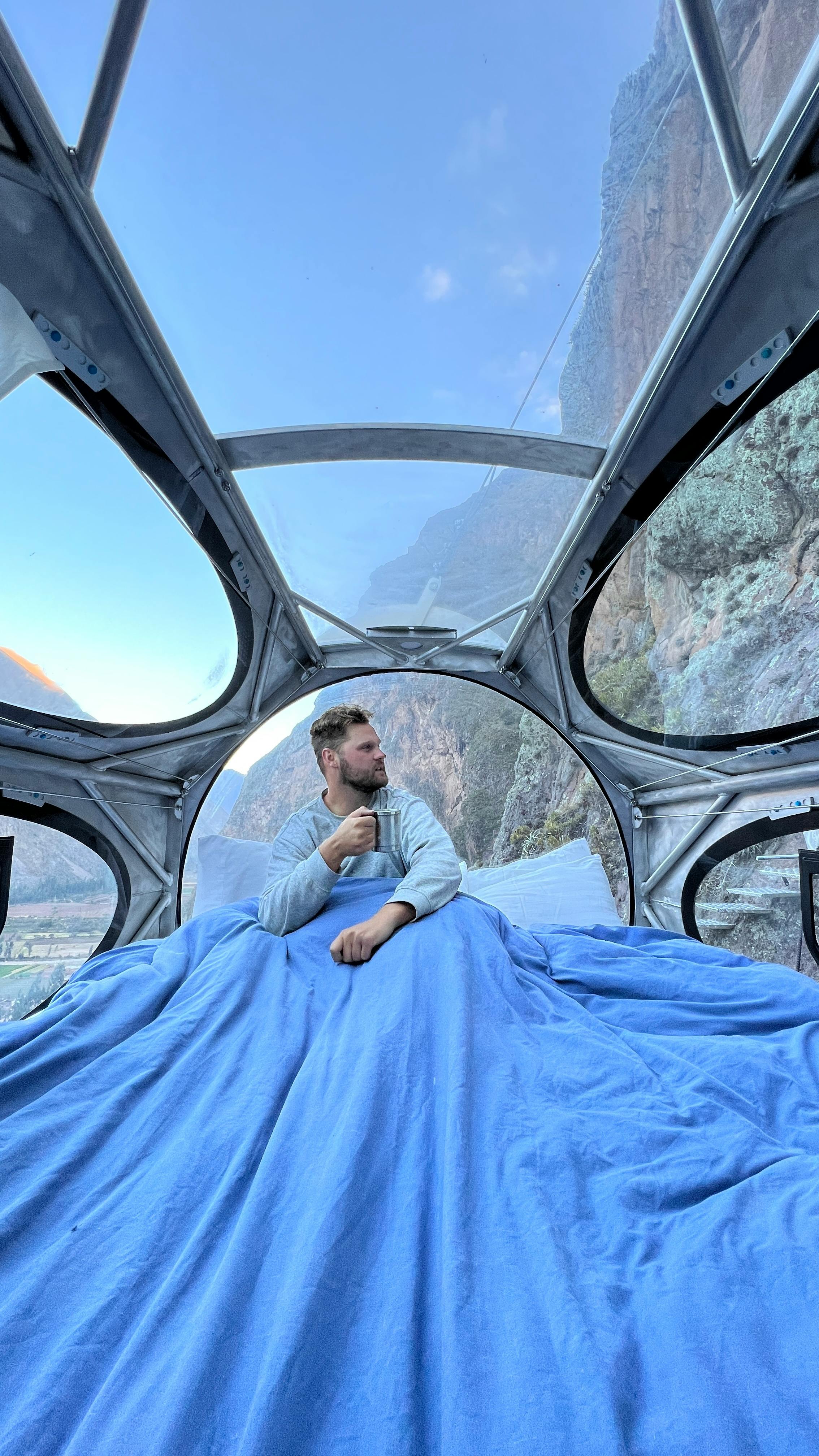 Man in transparent capsule hotel with stunning mountain views in Peru's Andes.
