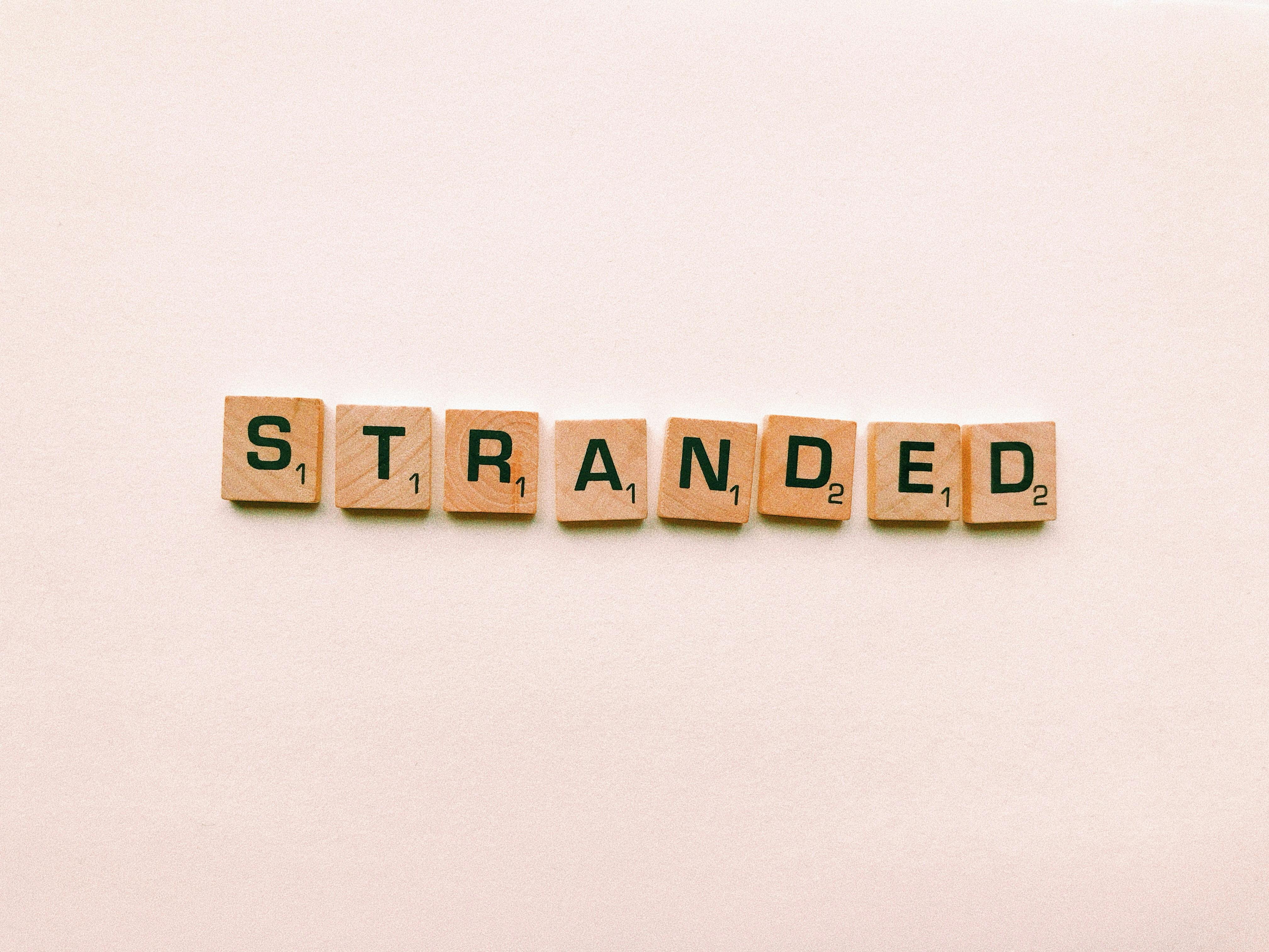 Wooden letter tiles spelling 'stranded' on a pink background, symbolizing isolation.